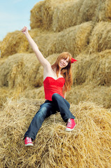 Naklejka na ściany i meble Happy smiling young girl sitting on a hay