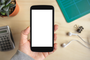Hand holding smartphone with isolated screen on wooden desk