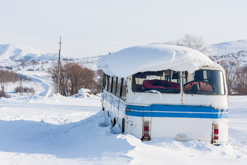 Old vintage bus covered with winter snow at mountains background