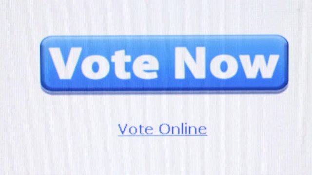 Macro close up camera dolly left to settle on large blue banner saying 'Vote Now', with text below stating 'Vote Online'. User clicks on banner, leading to 2nd voting page at end of clip.