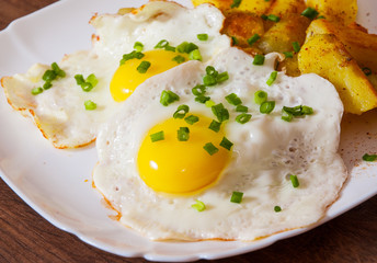 fried eggs with potato in a plate on wooden table