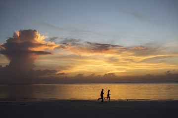 Silhouette of two people jogging on beach at sunrise