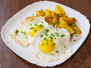 fried eggs with potato in a plate on wooden table