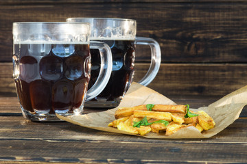 Two mugs of dark beer with fries
