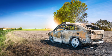automobile carbonizzata in un campo di periferia
