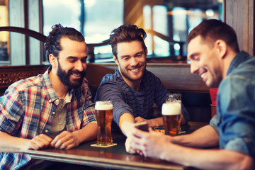 male friends with smartphone drinking beer at bar