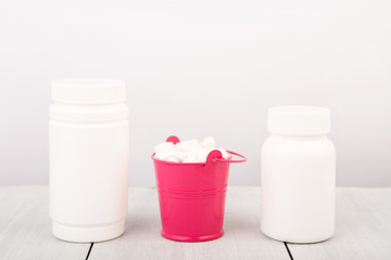 Many different white pills in a pink bucket and container 
