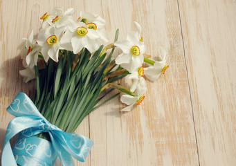 Narcissus bouquet decorated with a blue bow on a dark wooden planks, close up