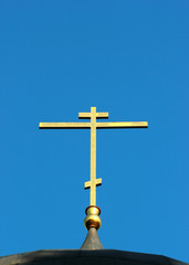 Golden cross on top of dome of russian orthodox church against blue sky background