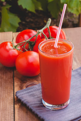 Glass of tomato juice with straw on wooden background