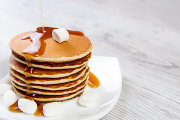 Tasty pancake on a white plate, wooden background, maple syrup