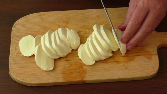 Sliced mozzarella with knife on wooden board 
