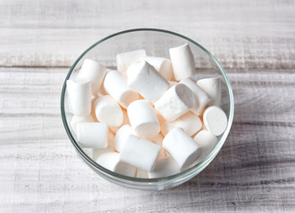 Marshmallows in glass bowl closeup on wooden background.