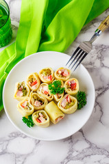 Pancakes rolls stuffed ham, pepper and salad, in bowl on marble background. 