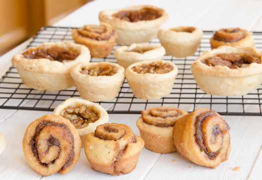 Freshly baked butter tarts and cinnamon rolls on a cooling rack