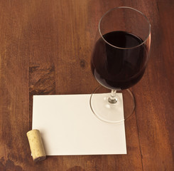 Red wine glass, white card, and cork on wooden texture