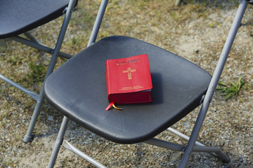 Red Sunday Missal on a folding chair outside. - obrazy, fototapety, plakaty