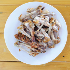 Chicken bones in white plate on wooden table, food scraps