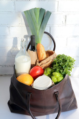 Tote (carry bag) with food products: bottle of milk, bottle of wine, leek, tomatoes, grapefruit, French baguette, basil, green paprika and bree chese.