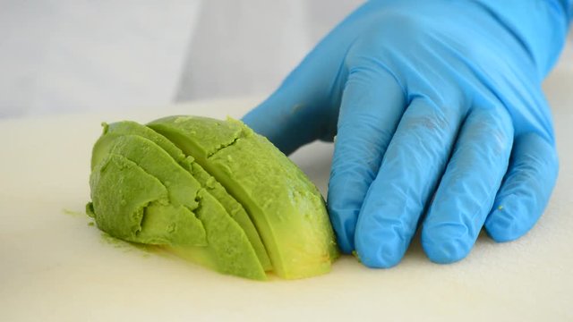 Hands of chef cutting a avocado fruit into slices with a knife in the kitchen for a recipe