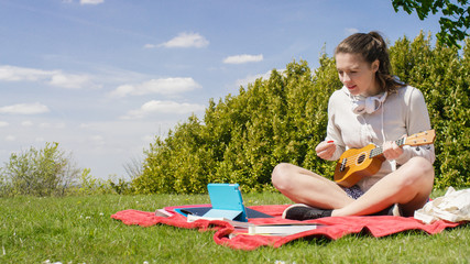 Obraz na płótnie Canvas Young woman learning how to play ukulele from a digital tablet tutorial