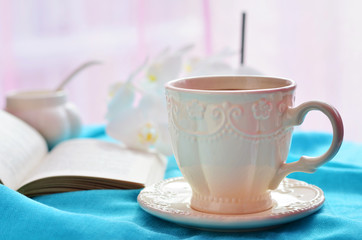 A cup of coffee, open book and flowers on a blue tablecloth