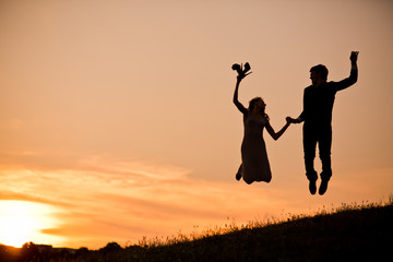 Young couple in love silhouette, a couple jump holding hands at the sunset. Romantic time in the sunset garden