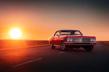 Vlies Fototapete Oldtimer Retro-rotes Auto, das bei Sonnenuntergang auf Asphaltstraße steht