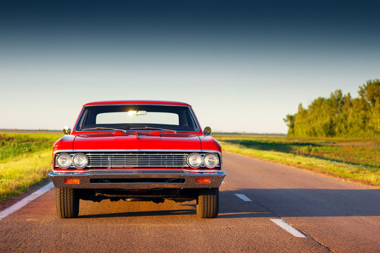 Retro red car standing on asphalt road at sunset