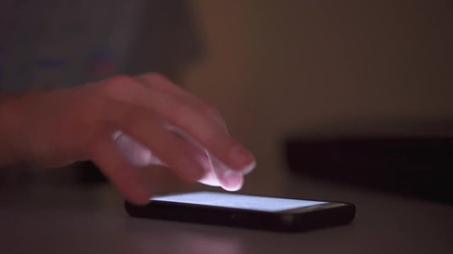 Person using cell phone in dark room scrolling through bright page on smart phone.
