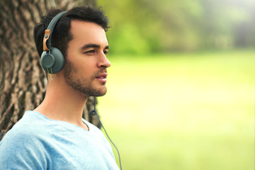 Portrait of beautiful dreaming young man with headphones, listen music on the tree background.