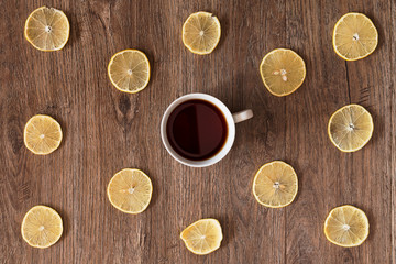 White cup of tea among the lemon slices on a wooden table. Top view.