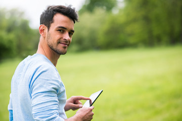 Young smiling business man with device on nature background look from his back