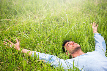 Happy beautiful man lying on the green grass with arms outstretched