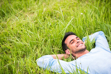 Naklejka na ściany i meble Smiling pretty young man lying, dreaming and relax on the green grass