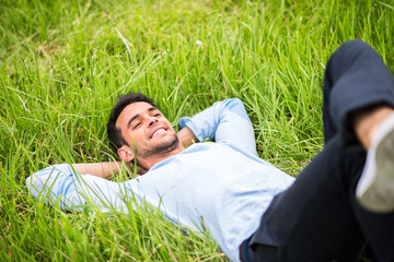 Naklejka na ściany i meble Beautiful young man lying, dreaming and relax on the green grass