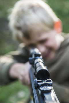 Portrait of little boy with airgun shooting outdoors, air rifle with telescopic sights