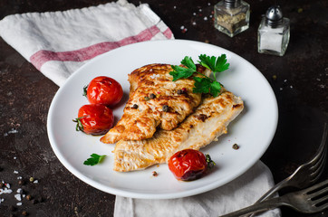 Roasted turkey cutlet or steak with tomatoes in white bowl on dark slate background. Selective focus