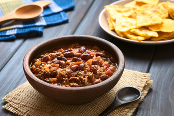 Chili con Carne bestehend aus Kidney-Bohnen, Hackfleisch, Tomaten und Zwiebeln, in rustikaler Schüssel, fotografiert mit natürlichem Licht (Selektiver Fokus, Fokus ein Drittel in den Chili)