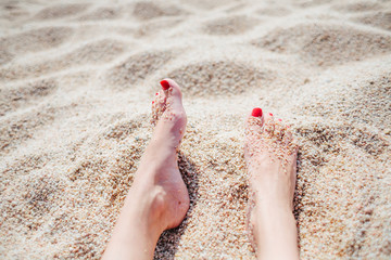 female feet with red pedicure in beach sand