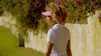 Young woman golfer posing in front of a wall covered in purple bougainvillea with her club over her shoulder smiling at the camera  side view