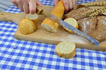 Someone cuts white baguette and dark bread with knife