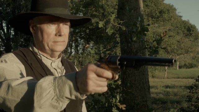 A cowboy from the American wild west era fires his black powder pistol
