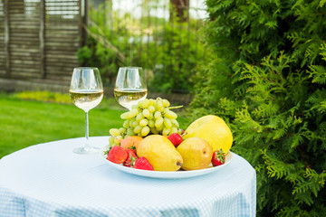 fresh fruit on a plate and wineglasses with white wine on a table in the garden