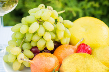 fresh fruit on a plate and wineglass with white wine on a table in the garden