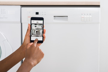 Woman's Hand Using Mobile Phone For Operating Dishwasher