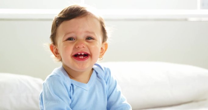 Cute baby with nightwear smiling and sitting on a bed