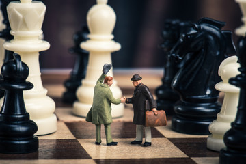 チェス盤の上で握手をしているミニチュアのビジネスマン
