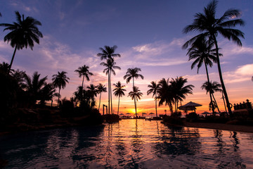 Fototapeta na wymiar Beautiful twilight on the beach with palm trees reflected in pool.