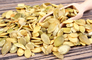 Pumpkin seeds with spoon on wooden background